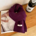 Detailed close-up view of luxury dark purple pure wool knit scarf texture and label. - Purple