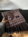 Vue en detail d'une écharpe à carreaux chaude en violet et marron avec franges et étiquette. - Violet