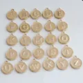 Detail view of gold-rimmed round enamel alphabet letter charms, A to Z DIY jewelry pendants. - Light Brown