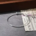 Close-up detail of a minimalist silver adjustable metal coil bangle bracelet on dark surface. - Silver