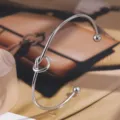 Primer plano de un brazalete abierto de acero de titanio minimalista con detalle de nudo. - Color acero