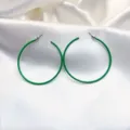 Detail van grote groene metalen gelakte oorbellen met een gladde afwerking en stijlvol design. - Groen
