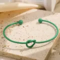 Groene metalen knoop open armband, elegante detailfoto met uniek getwist ontwerp. - Zeegroen