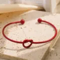 Rode open metalen armband met stijlvol knoopdesign en baluiteinden op een stenen achtergrond. - Bordeauxrood