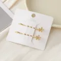 Ensemble de pinces à cheveux dorées avec fleurs en zircon scintillant sur carte blanche. - Fleur Or