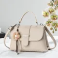 Nahaufnahme der eleganten beige Handtasche mit zartem Blumenanhänger und Metall. - Hellbeige