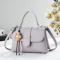 Elegante violette Lederhandtasche mit Henkel, schickem Blumenanhänger und Umhängegurt. - Lila