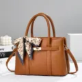 Elegant brown leather handbag featuring a stylish patterned scarf and chic gold-tone lock detail. - Earthy Yellow