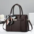 Detailed view of the elegant dark brown handbag with stylish scarf and gold-tone turn-lock hardware. - Coffee