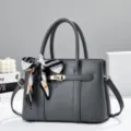 Dark grey women's handbag with top handle, shoulder strap and chic patterned scarf accent. - Gray