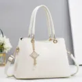 Nahaufnahme einer weißen Mode-Umhängetasche mit goldener Hardware und elegantem Kettenanhänger. - 28x13x20cm / Weiß