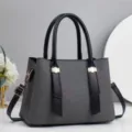 Detailansicht der eleganten grauen Damenhandtasche mit schwarzen Henkeln und goldener Hardware. - 28x13x20cm / Schwarz