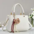 Detailaufnahme der weißen PU-Ledertasche mit goldenen Beschlägen und süßem Bären-Plüschhänger. - Weiß