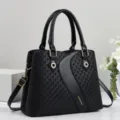 Detail shot of black woven leather handbag featuring dual top handles and adjustable shoulder strap. - Black