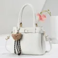 Detailansicht der eleganten weissen Lederhandtasche Textur und dem niedlichen Baer Anhaenger. - L27 B13 H20 Griff 18cm / Weiß