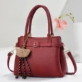 Detailansicht der weinroten Litschistruktur Leder Handtasche mit Bärenanhänger und Schnalle. - L27 B13 H20 Griff 18cm / Rot