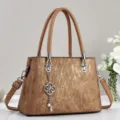 Detailed close-up view of brown textured retro handbag featuring metal clover charm and shoulder strap. - Khaki