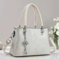 Nahaufnahme der eleganten cremefarbenen Handtasche mit edlem Metallanhänger und Textur. - Weiß