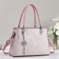 Nahaufnahme der rosa Damentasche mit eleganten vertikalen Streifen und Metall-Kleeblatt-Anhänger. - Rosa