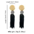 Close-up detail view of bohemian long tassel earrings with stylish gold disc and black fringe element. - Earrings / Gray