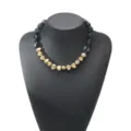Detail view of the elegant black and gold irregular resin beaded statement necklace piece. - Black