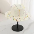 Close-up of flat top straw hat with colorful paint splatter design for summer beach wear. - M (56-58cm) / Cream