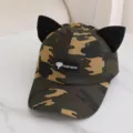 Vista detallada de una gorra de béisbol de camuflaje con orejas de gato y etiqueta artesanal. - Talla Única para Adultos / Camuflaje