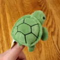 Green turtle finger puppet plush toy close-up detail shot, soft fabric, cute animal design. - Turtle Finger Puppet