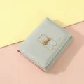 Close-up view of a mint green mini wallet featuring a cute bear outline and golden bow detail. - Light Green