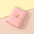 Detailopname van roze lederen portefeuille met schattig beren- en strikdetail. - Roze
