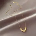 Vue détaillée du collier élégant en acier au titane doré avec des pendentifs perles étincelants. - Or
