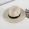 Vista detallada de un elegante sombrero de paja beige con cinta negra sobre una superficie limpia. - M (56-58cm) / Beige