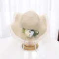 Gros-plan d'un chapeau de paille à large bord avec décoration florale, bordure en filet et rubans. - M (56-58cm) / Beige