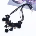 Close-up detail of black layered fabric flower necklace with pompoms and tassels. - Black