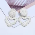 Close-up detail of white floral embossed heart earrings showcasing intricate metallic craftsmanship. - White