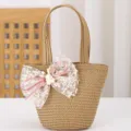 Detalle del bolso de paja con lazo de encaje blanco, cintas rosas y adorable adorno de conejito. - Caqui