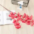 Vue détaillée d'une branche de fleurs de cerisier artificielles roses sur fond bois. - Rose rouge