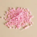 Primo piano di perline di semi di gelatina rosa da 3mm sparse con uno spillo dorato per gioielli. - Stile 03