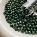 Macro detail of green faceted fire polished glass beads spilling from tube on white plate. - Style 06 / 10 Pieces/Pack