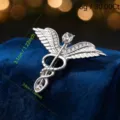 Broche vintage de plata con pedrería alas y caduceo, elegante alfiler de metal y cristal. - Plateado