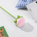 Nahaufnahme Detail einer handgehäkelten rosa Rose mit grünem Stiel für die Raumdeko. - Hellrosa