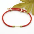 Gedetailleerde close-up van een rode gevlochten armband met gouden metalen onderdelen. - Rood