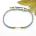 Detailed close-up of a blue-gray braided rope bracelet with polished gold metal accessories. - Blue Gray