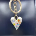 Close-up gold keychain with enamel heart pendant, colorful artistic eye and flower doodle details. - Style R