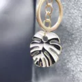 Close-up detail of stylish black and white enamel monstera leaf key ring alloy bag charm pendant. - Style Q