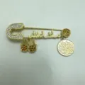 Close-up detail of a gold-toned rhinestone safety pin brooch with hamsa hand and coin charms. - Golden Yellow Series