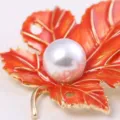 Macro detail shot of orange enamel maple leaf brooch featuring white pearl inlay and gold tone. - Orange Red