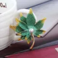 Gros plan détaillé sur l'élégante broche feuille d'érable vert-or avec une perle centrale. - Feuille d'Érable Vert Doré