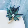Gros plan détaillé d'une broche élégante en forme de feuille d'érable avec perle centrale. - Feuille d'Érable Bleu