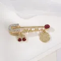 Elegante spilla di sicurezza dorata con strass scintillanti e ciondoli pendenti chic. - Stile Rosso Scuro